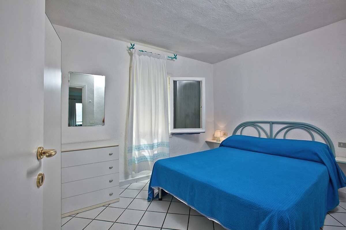 A bedroom with a bed, a dresser, a mirror, a window, and a curtain.