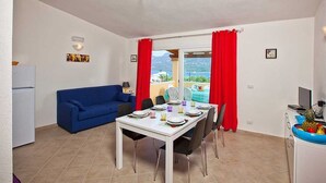 Un espacio habitable compacto con comedor, un sofá azul, un refrigerador blanco y vistas a una piscina y montañas.