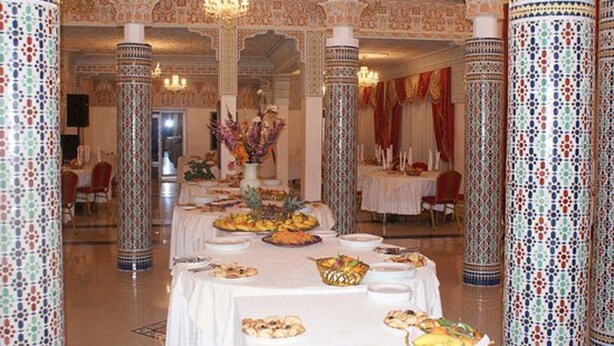 Un salón de banquetes con columnas ornamentadas, mesas dispuestas para una comida y candelabros.