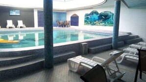 Piscina interior con escalones revestidos que bajan al agua, sillas de descanso y un mural con motivos de peces en la pared.