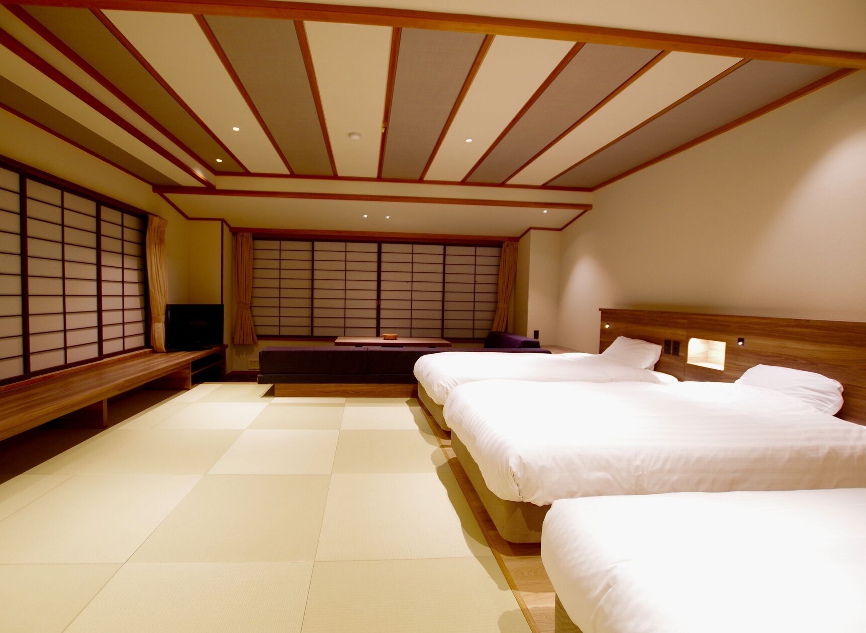 A traditional Japanese-style bedroom with tatami flooring, a futon bed, a wooden headboard, and shoji screens.