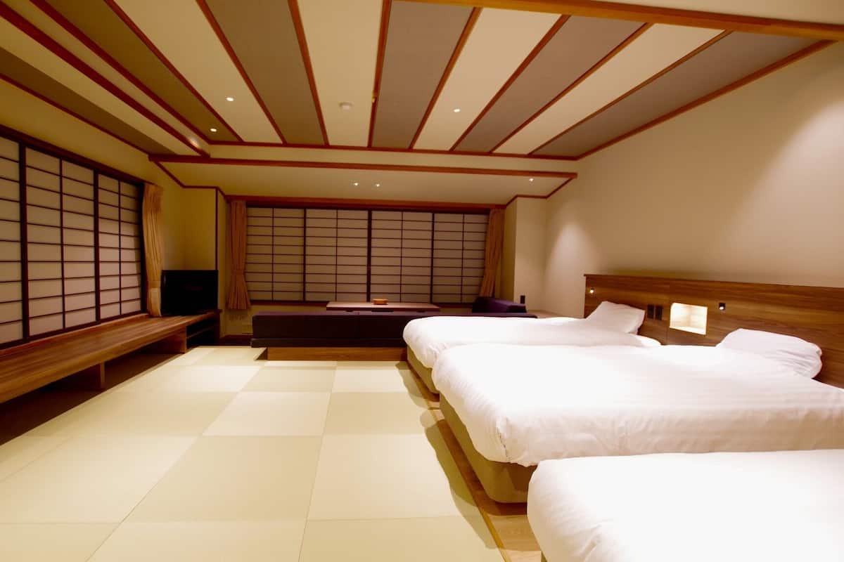 Une chambre de style japonais traditionnel, avec un sol recouvert de tatamis, un futon, une tête de lit en bois et des paravents shoji.