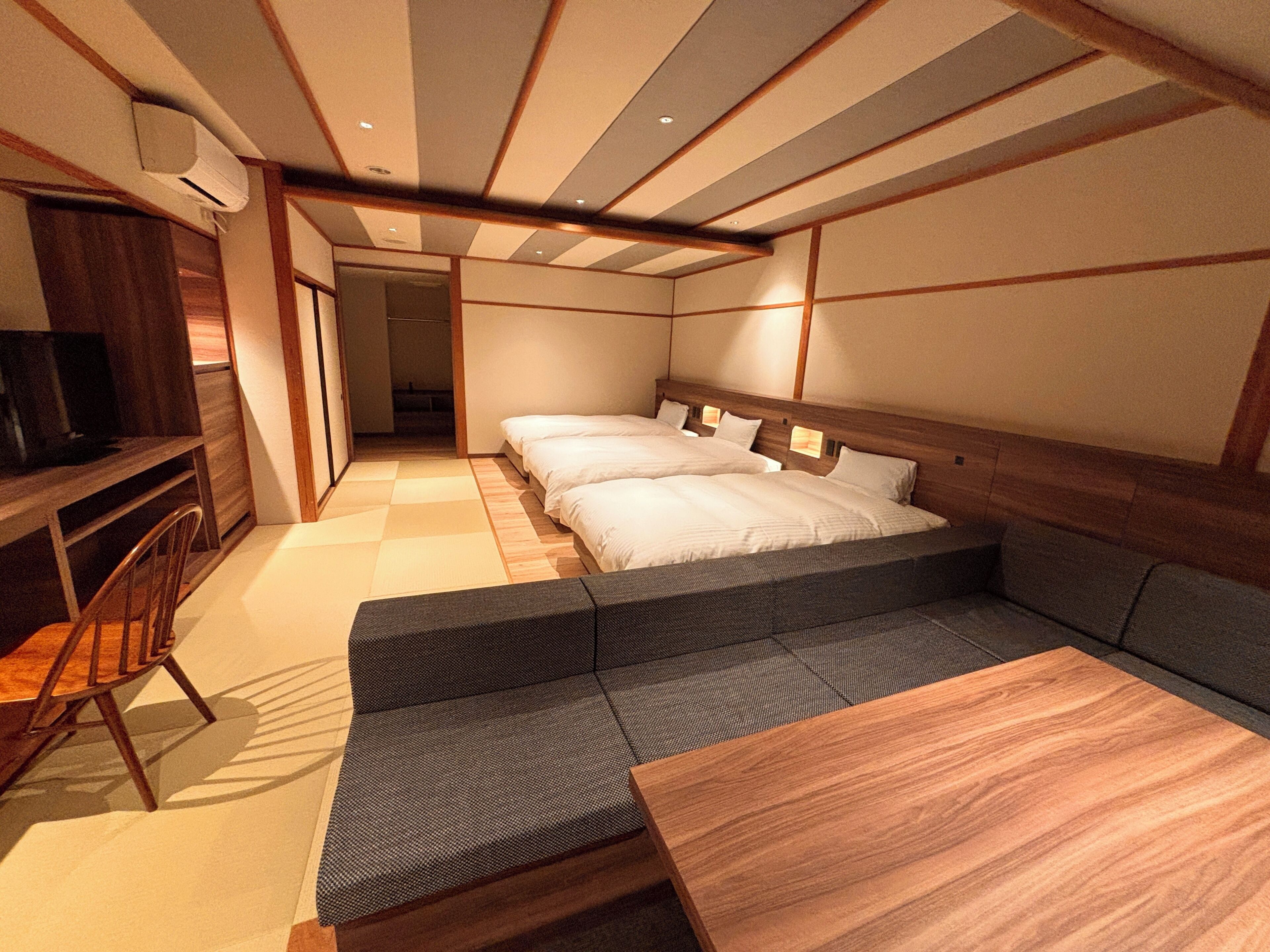 A room with two beds, a sofa, a TV, and a wooden table.