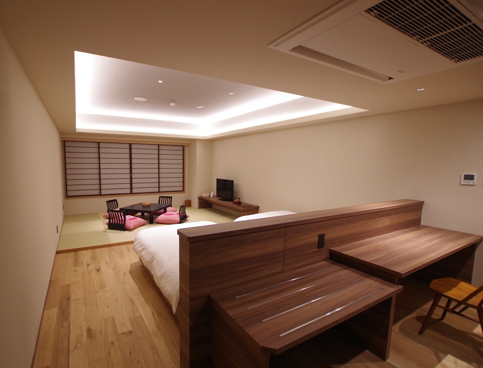 A modern bedroom with a bed, a desk, and a TV.