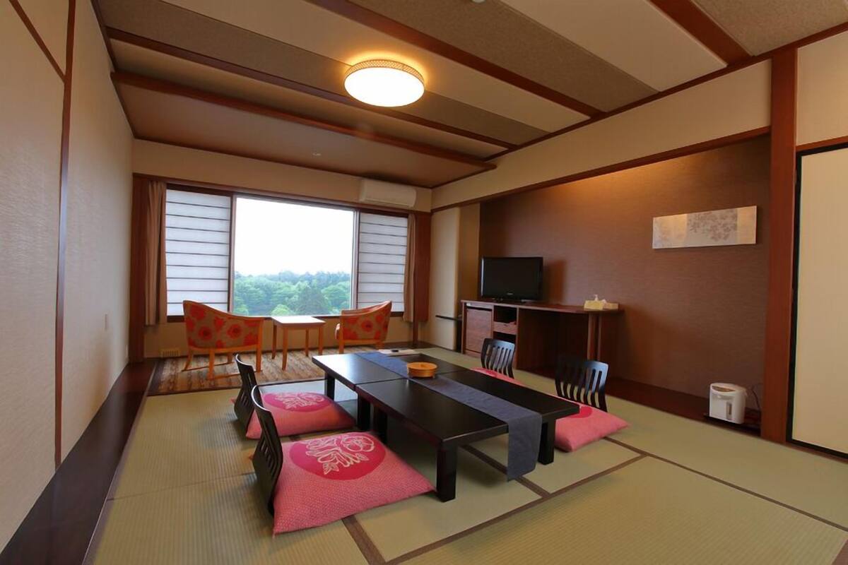 Une pièce de style japonais traditionnel, avec un sol recouvert de tatamis, une table basse, des chaises, un téléviseur et une vue par la fenêtre.