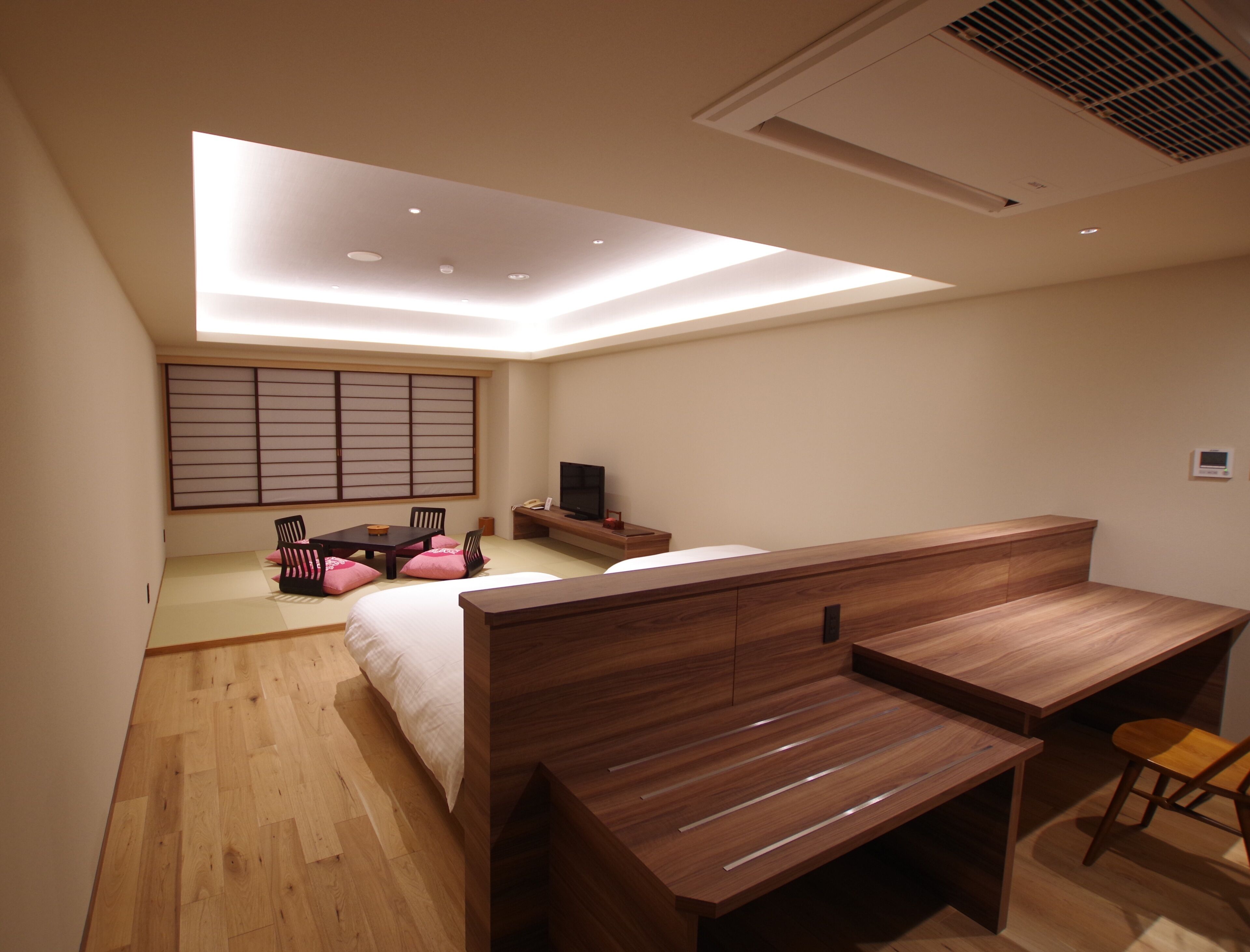 A modern bedroom with a bed, a desk, and a TV.