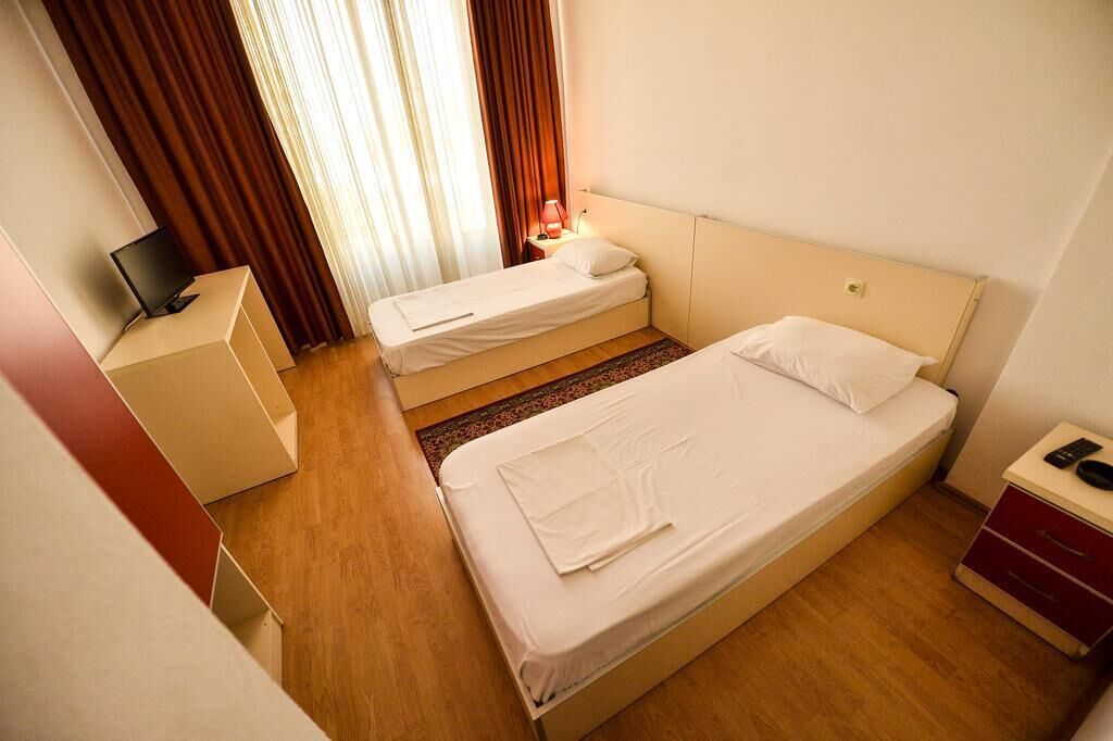 Habitación de hotel con dos camas individuales, un escritorio con ordenador y una mesita de noche con lámpara.
