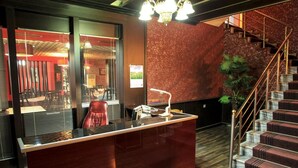 A reception area with a marble counter, a red chair, a staircase with a railing, and a potted plant.