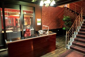 Ein Empfangsbereich mit einer Marmor-Theke, einem roten Sessel, einer Treppe mit Metallgeländer und einem Blumentopf.