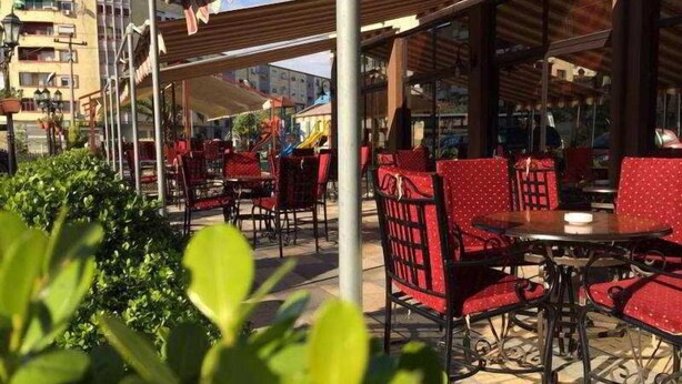 An outdoor seating area with tables and chairs, surrounded by greenery.