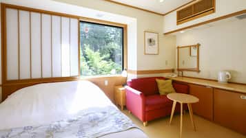 Een hotelkamer met een bed, een rode bank, een klein tafeltje, een spiegel en een raam met uitzicht op bomen.