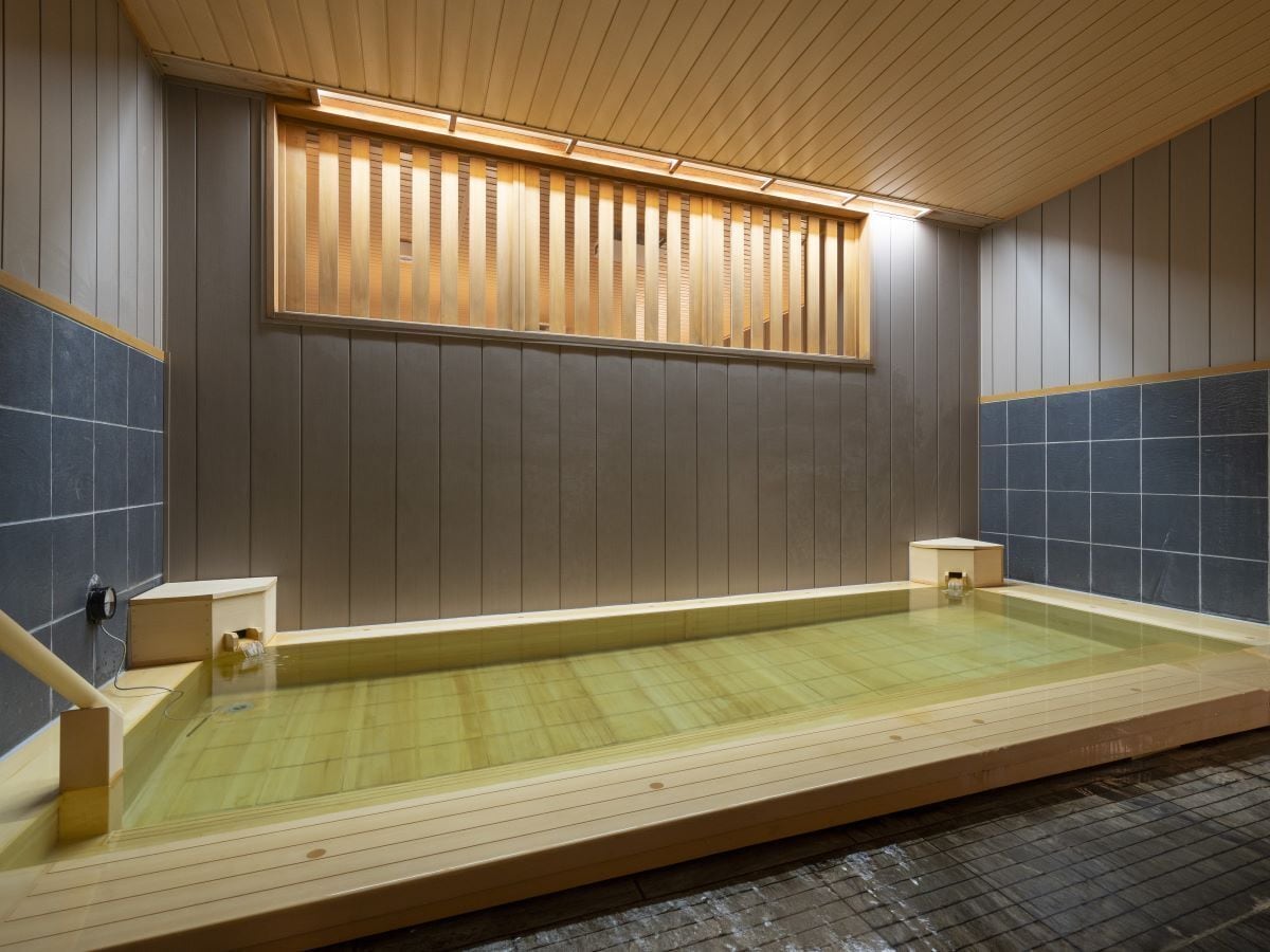 A traditional Japanese onsen with a wooden deck, a small wooden bench, and a tiled wall.