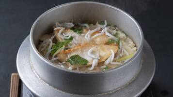 A bowl of soup with noodles, vegetables, and a piece of meat on a dark surface.