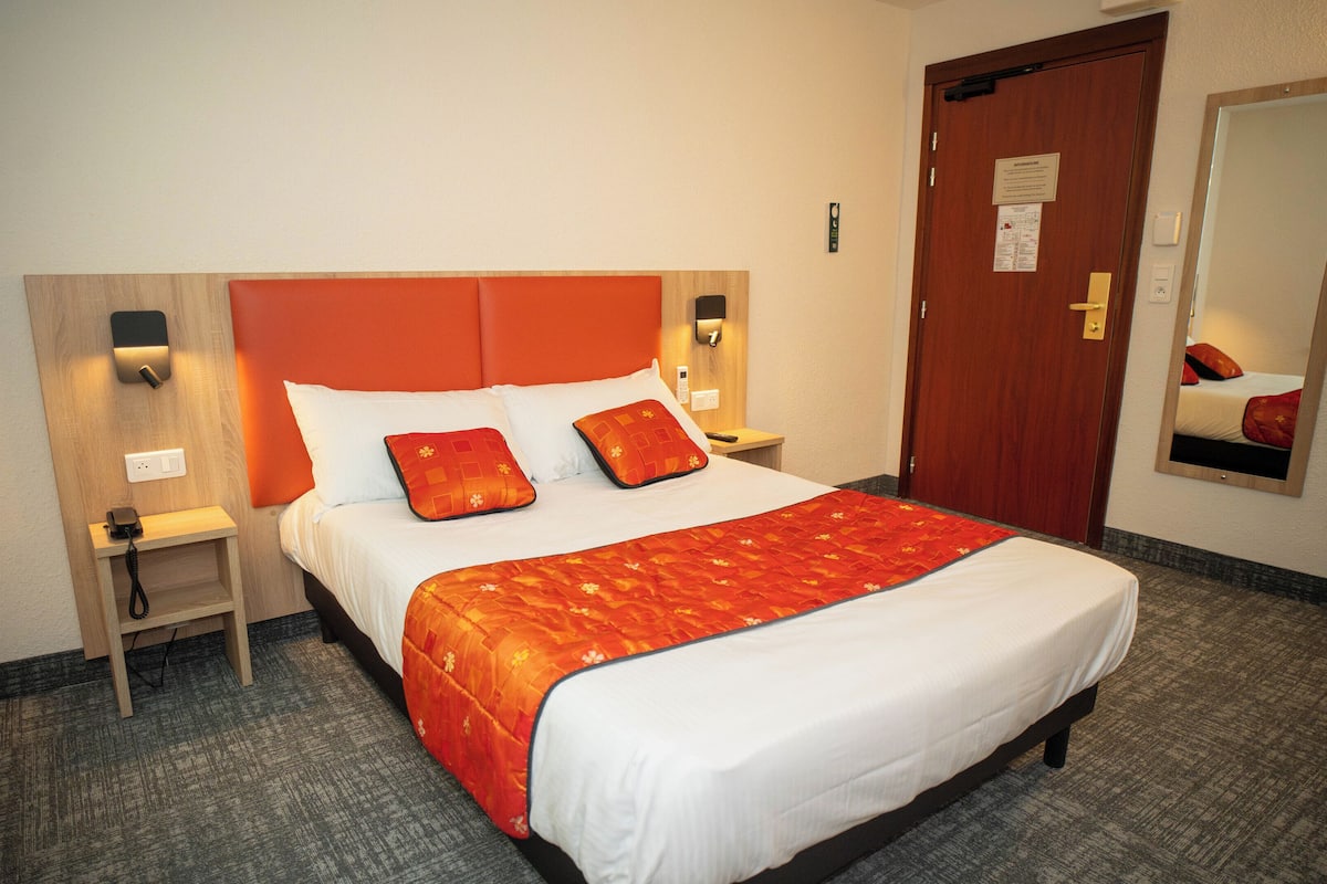A hotel room with a large bed, two bedside tables, a nightstand, a mirror, and a door with a lock.