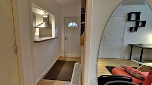 A narrow hallway leading to a compact living space with a kitchenette, a door with a window, and a small seating area with a red couch. - Hôtel de l'île (Custines)