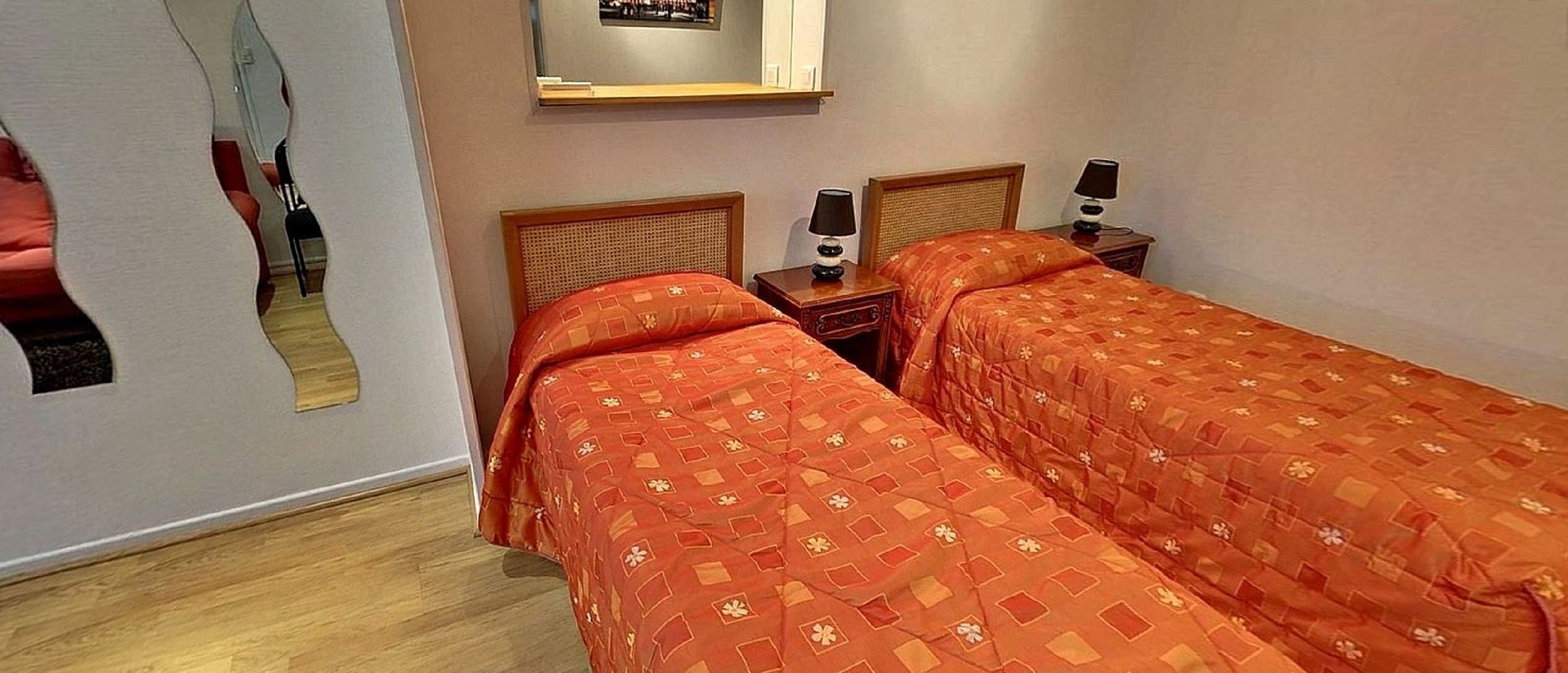 Une chambre d’hôtel avec deux lits, chacun recouvert d’une couvre-lit à motifs, une table de chevet avec une lampe et un miroir au mur.