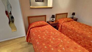 Una habitación de hotel con dos camas, cada una con una colcha estampada, una mesita de noche con lámpara y un espejo en la pared.