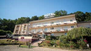 A multi-story hotel with balconies, a staircase leading to the entrance, and a garden with flowers. - Hôtel de l'île (Custines)