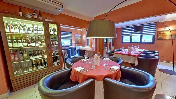 A restaurant with round tables, black leather chairs, and a wine display cabinet. - Hôtel de l'île (Custines)