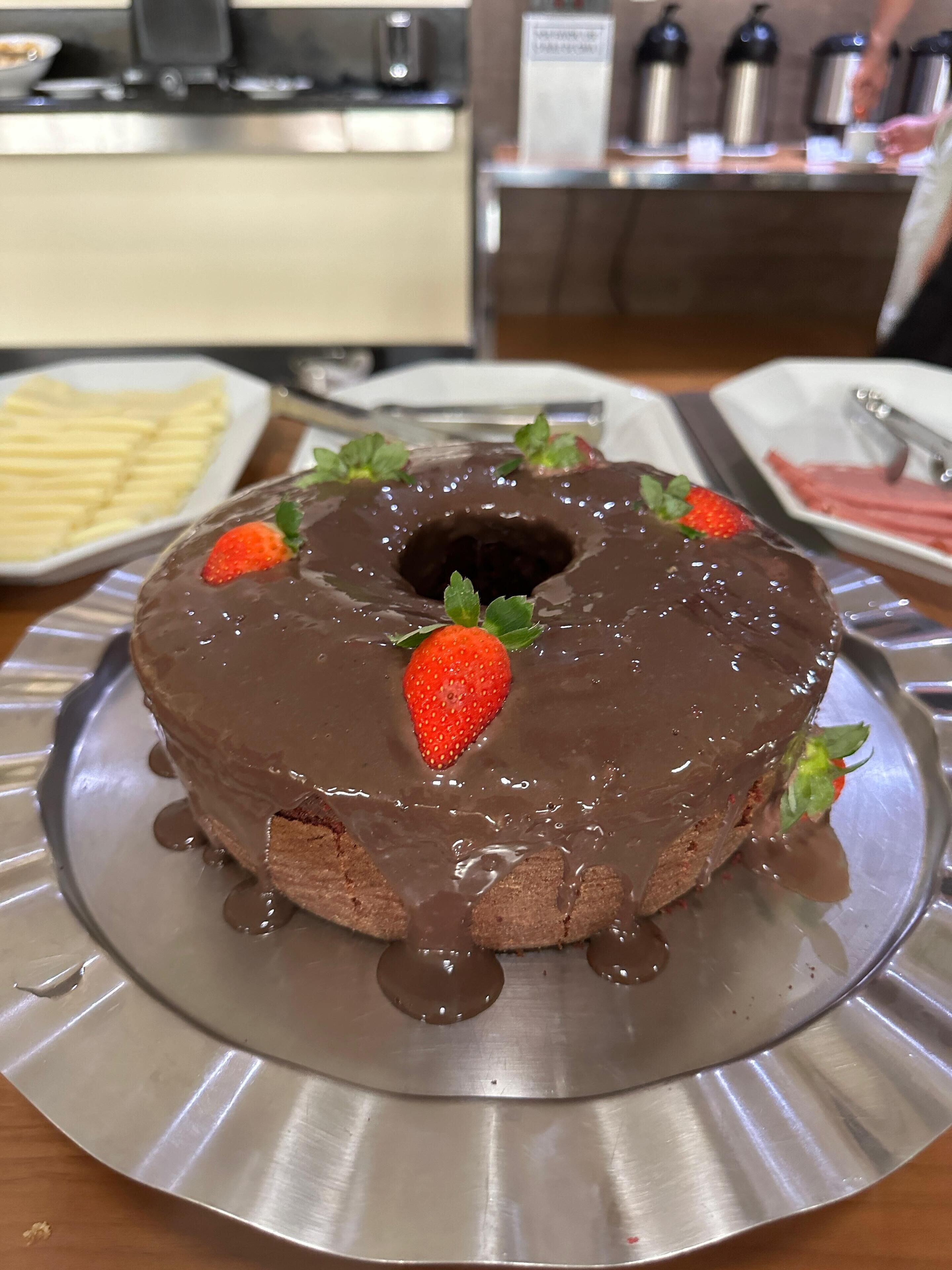 A chocolate bundt cake with strawberries on a metal plate.