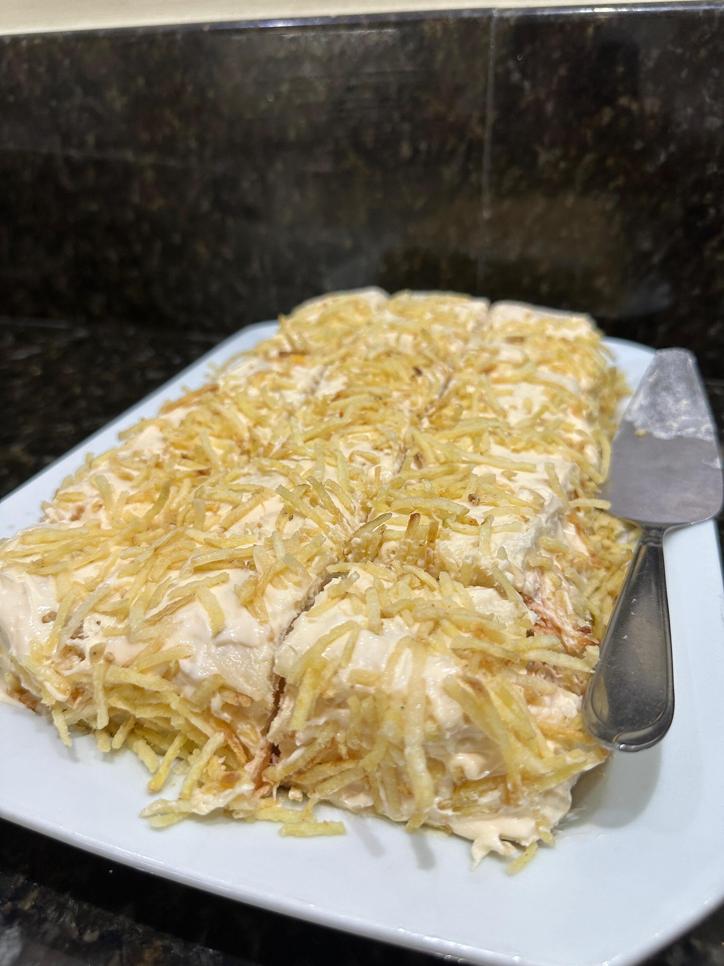 A white plate with a food item covered in shredded cheese and a spatula on the side.