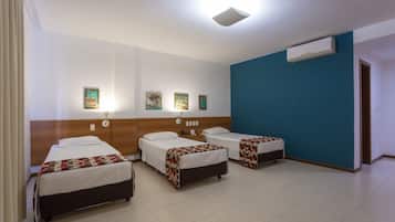 Habitación de hotel con tres camas individuales, cabecera de madera, pared de acento azul y un equipo de aire acondicionado.