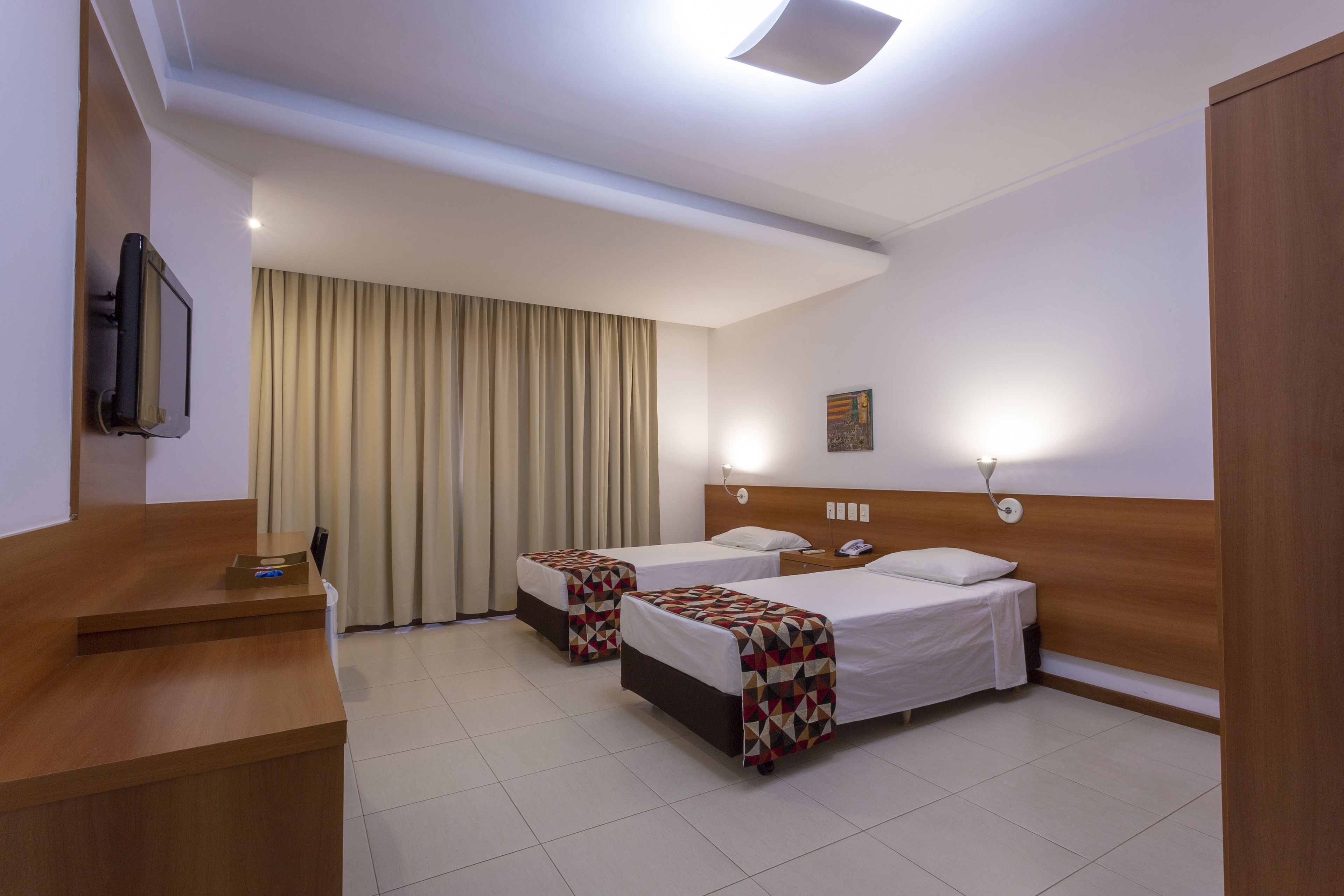 Habitación de hotel con dos camas, un escritorio, un televisor y una ventana con cortinas.