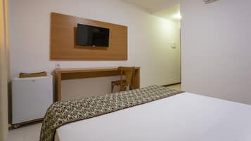 Quarto de hotel com cama, escrivaninha, cadeira, televisão fixada na parede e ar condicionado.
