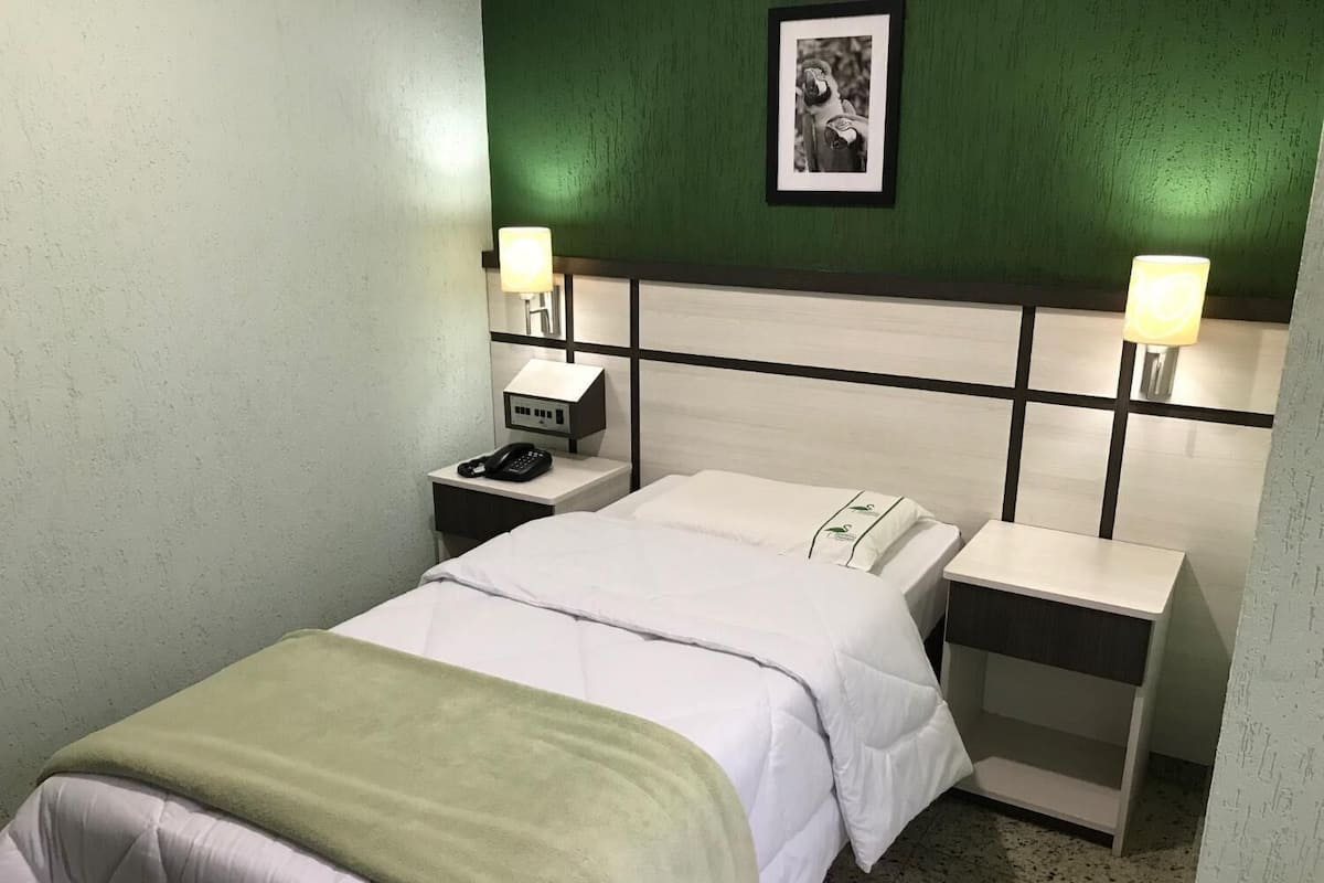 Ein Hotelzimmer mit einem Bett, zwei Nachttischen, einem Beistelltisch mit Telefon und einem gerahmten Bild an der Wand.