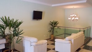 Un salon avec deux canapés blancs, un téléviseur à écran plat, un lustre et des plantes en pot.