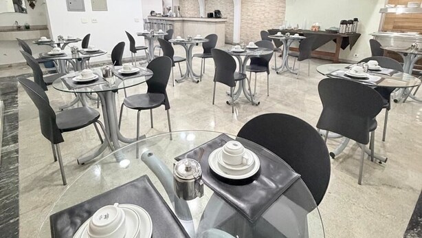 Un espace repas moderne avec des tables rondes, des chaises noires et une cuisine en arrière-plan.