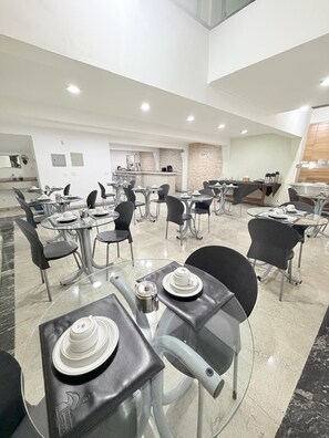 A modern dining area with round tables, black chairs, and a kitchen in the background. - Hotel Pantanal Santa Cruz (São Paulo)