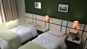 Une chambre d’hôtel avec deux lits, chacun étant équipé d’un oreiller et d’une couverture. Il y a des tables de chevet avec des lampes et un téléphone. Les murs sont verts et des tableaux encadrés y sont accrochés.