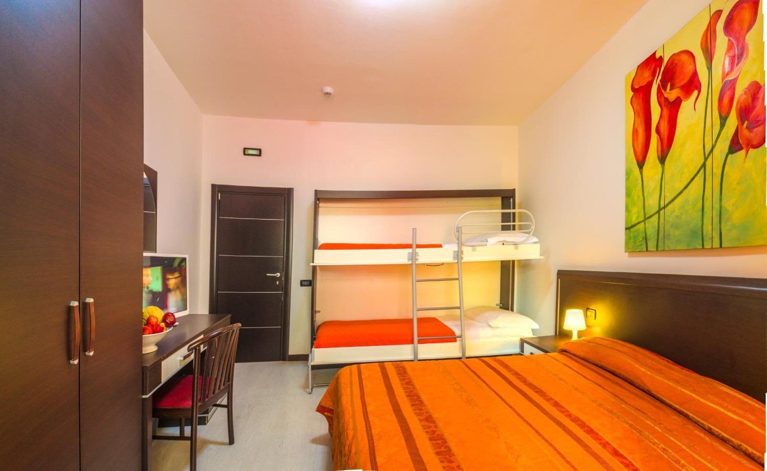 Habitación de hotel con literas, un escritorio con silla, un armario y un cuadro en la pared.