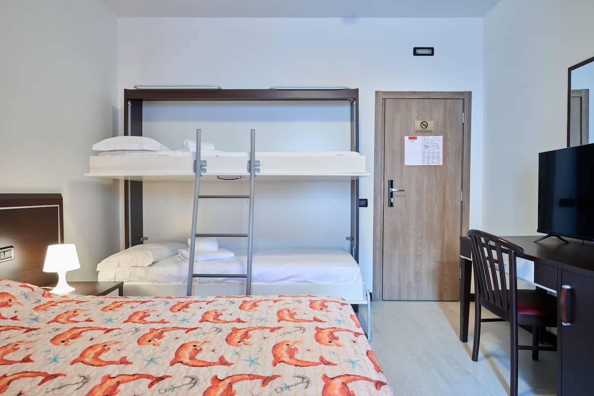 Una habitación de hotel con literas, un escritorio, una silla, un televisor y una lámpara de noche.