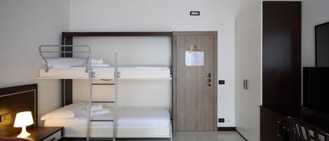 A hotel room with bunk beds, a desk with a lamp, a TV, and a wardrobe.