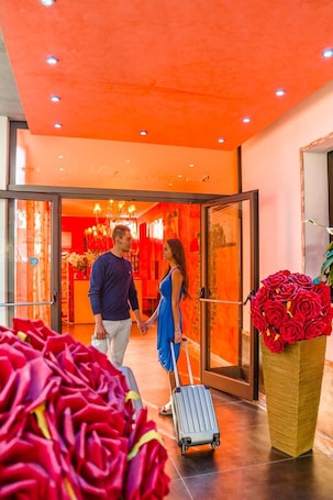 A hotel lobby with a bright orange ceiling, a large vase of red roses, and a person pulling a suitcase.