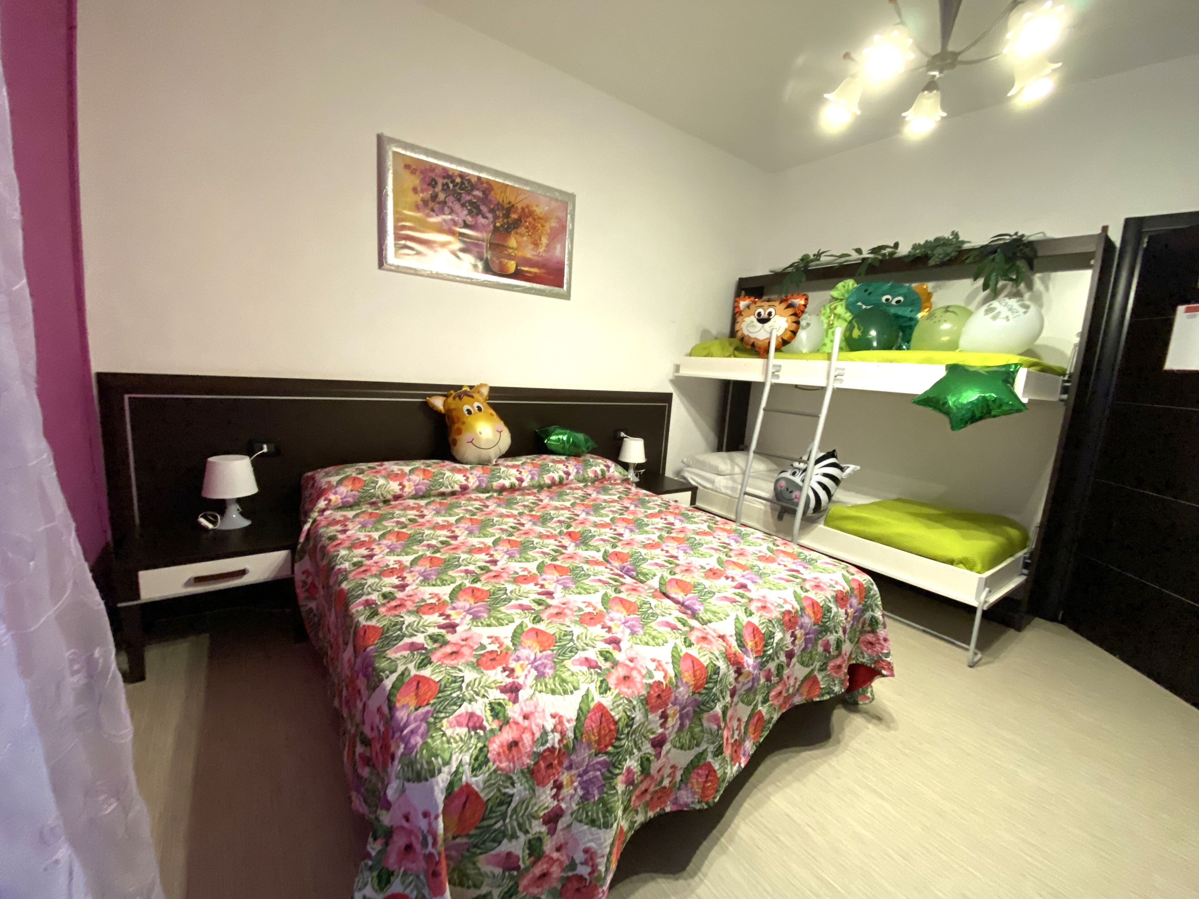 A bedroom with a floral bedspread, a giraffe-shaped pillow, a painting on the wall, and a bunk bed with green pillows.