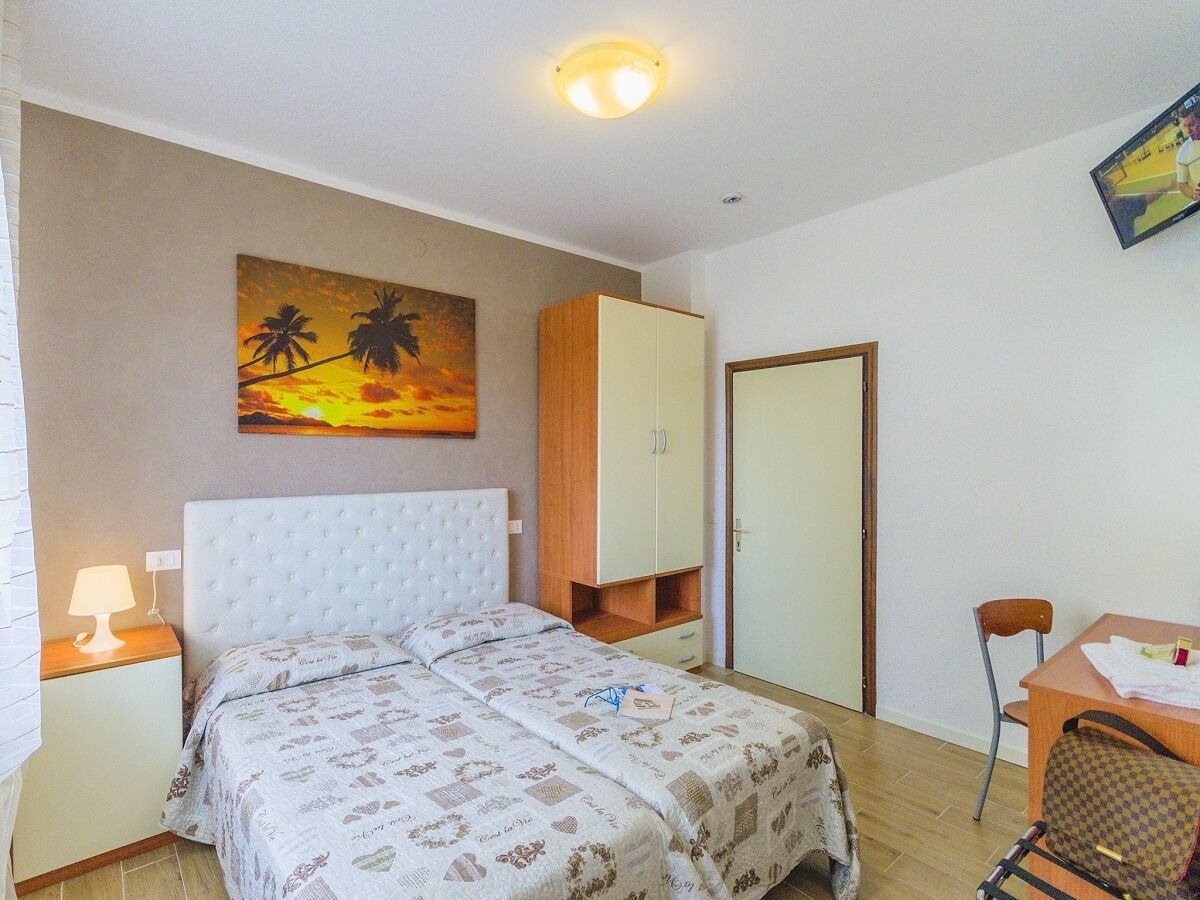 A bedroom with a bed, a nightstand, a desk, a chair, a wardrobe, and a painting on the wall.