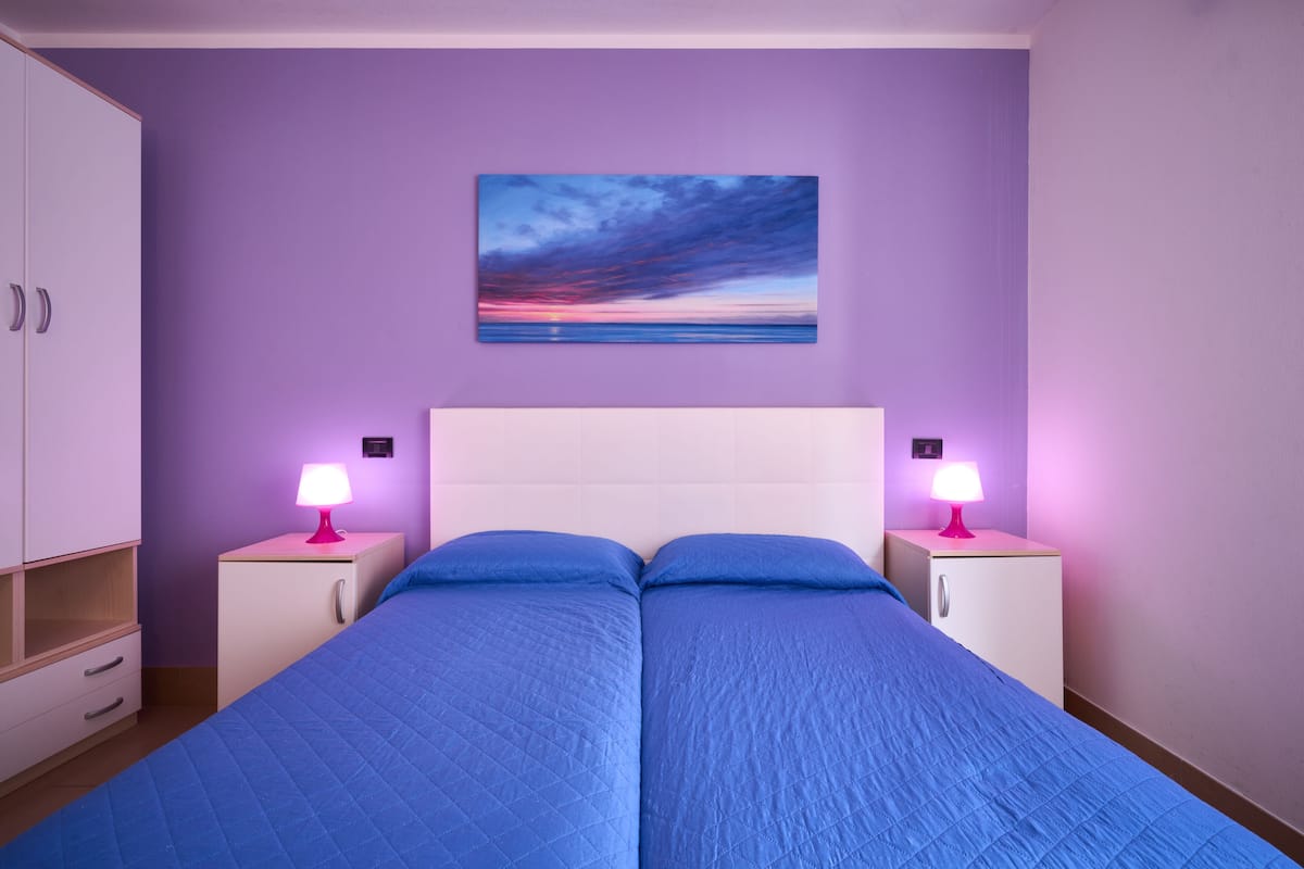 Un dormitorio con dos camas, una mesita de noche con lámpara, un armario y un cuadro en la pared.