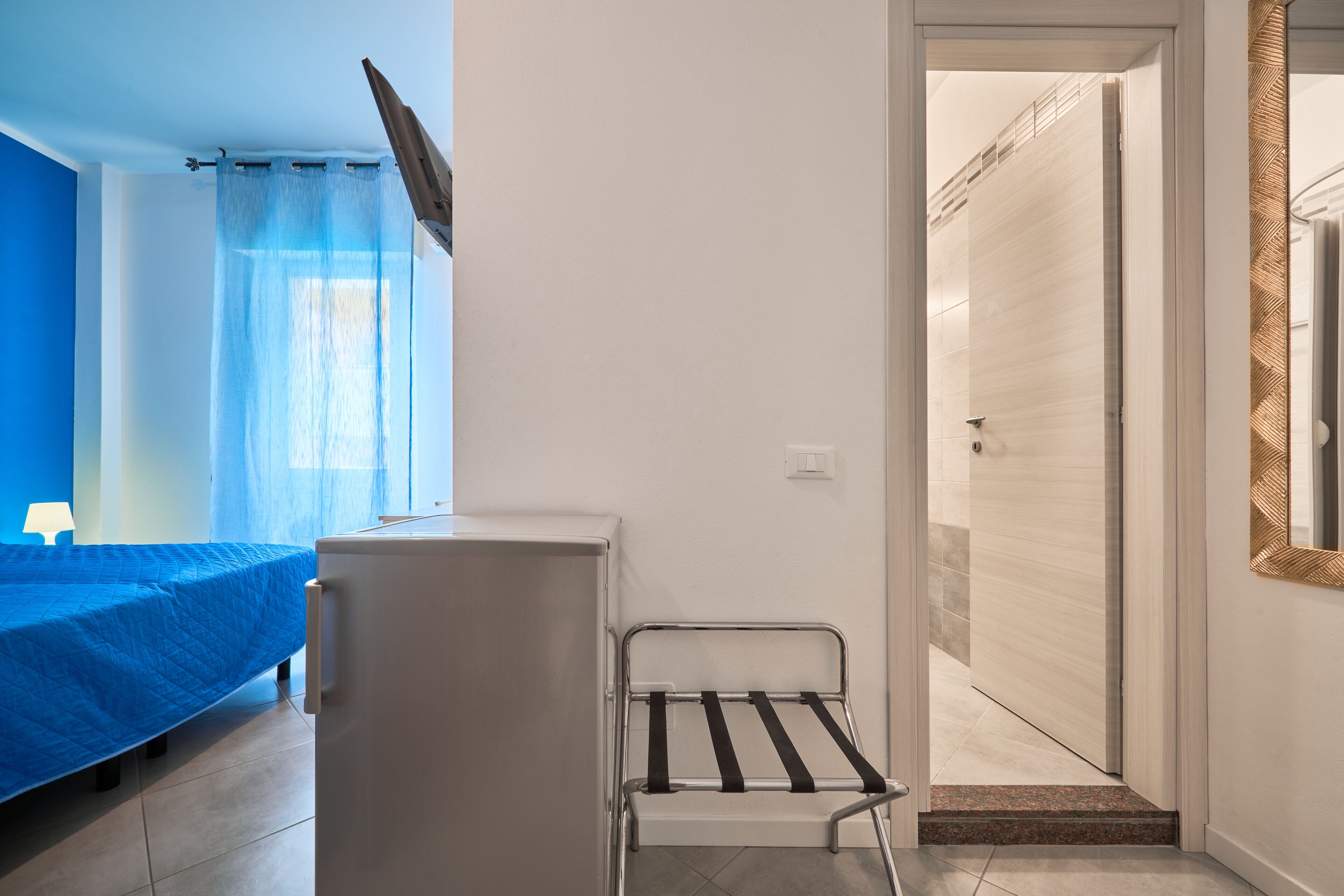 A compact room with a bed, a small white cabinet, and a metal drying rack.