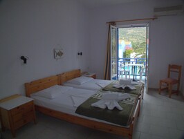 Un dormitorio con dos camas, cabecero de madera, mesita de noche, una silla y un balcón con vistas.