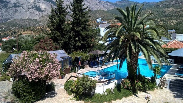 A pool area with a mountain backdrop, surrounded by greenery and a few buildings. - Hotel Sofia (Samos)