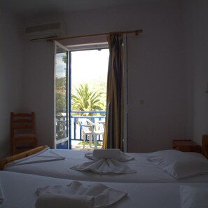 A hotel room with a bed, a chair, and a view of a balcony with a palm tree. - Hotel Sofia (Samos)