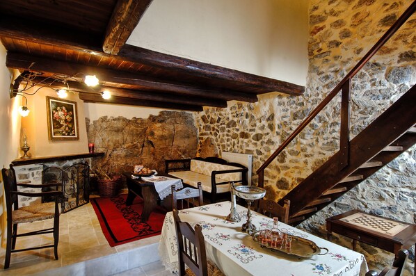 A rustic dining area with stone walls, wooden beams, and a red carpet. - Thalori (Gortyna)