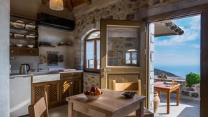 A kitchen with a stone wall, wooden cabinets, and a view of the sea. - Thalori (Gortyna)