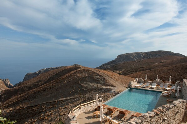 A pool area with lounge chairs and umbrellas, surrounded by rocky terrain and a view of the sea. - Thalori (Gortyna)