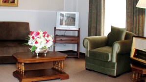 A living room with a brown sofa, a green armchair, a wooden coffee table with a vase of flowers, a television on a stand, and a framed picture on the wall. - Coloso Potosi (Potosi)