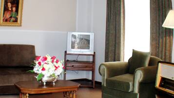 Ein Wohnzimmer mit einem braunen Sofa, einem grünen Sessel, einem Holztisch mit Blumen in einer Vase, einem Fernseher auf einem Schrank und einem gerahmten Bild an der Wand.
