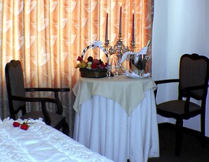 Una mesa de comedor dispuesta con una cesta de frutas, una jarrón y un candelabro. Dos sillas se encuentran alrededor de la mesa.